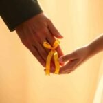 Manos entrelazadas en gesto de apoyo con un lazo amarillo simbolizando la prevención del suicidio